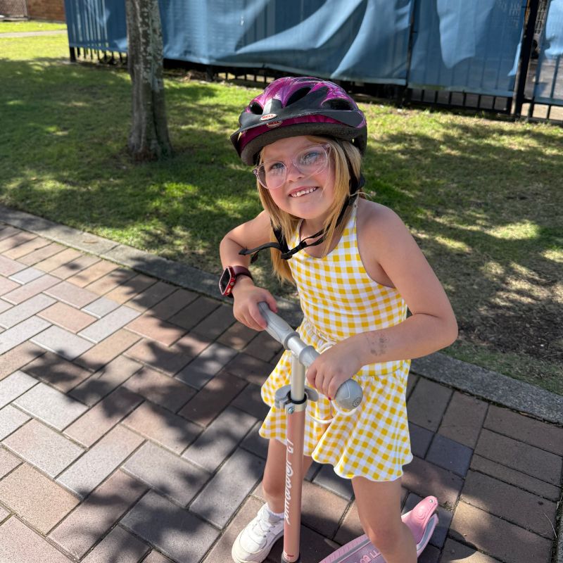 Young girl wears a helmet and stands over a scooter