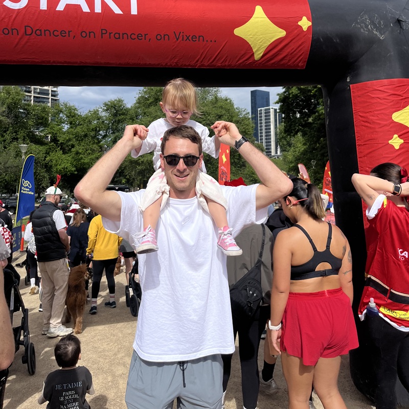 Young girl sits on top of her dad's shoulders at the Santa Fun Run start line