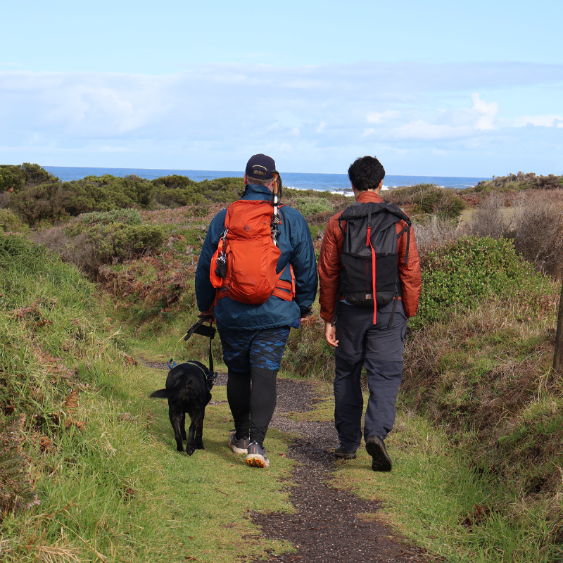 Dale Piece walks along a grassy path with his Seeing Eye Dog and tour guide at the great ocean walk
