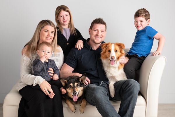 A family portrain of two parents, three kids and two dogs on a chaise lounge