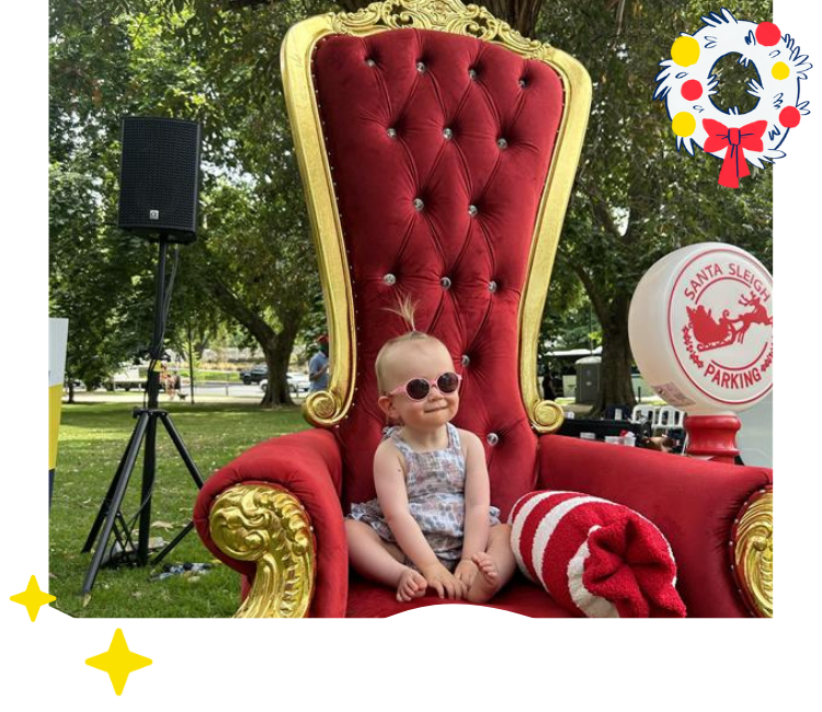 Vision Australia client Sienna smiles for a photo sitting on Santa's throne.