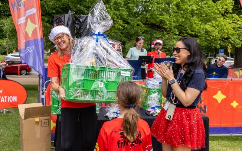A lady wearing a Santa Hat holds a large package wrapped in cellophane at Santa Fun Run