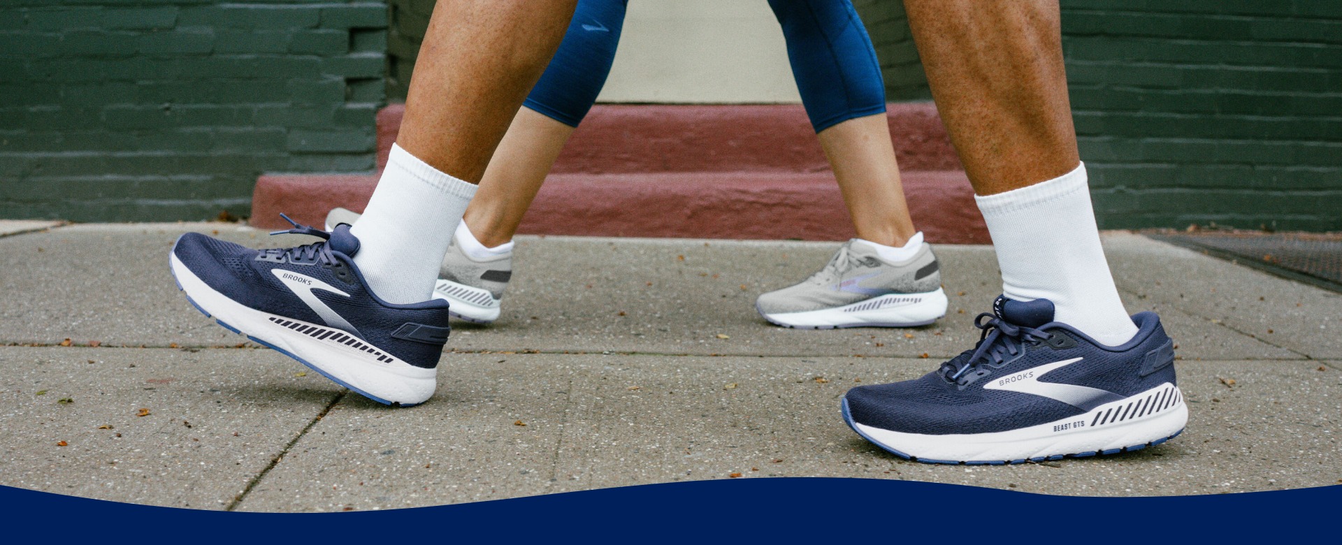 Feet of two people walking wearing Brooks sneakers