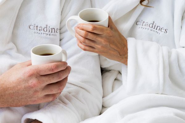 Two people wearing Citadines robes sit next to eachother holding white mugs