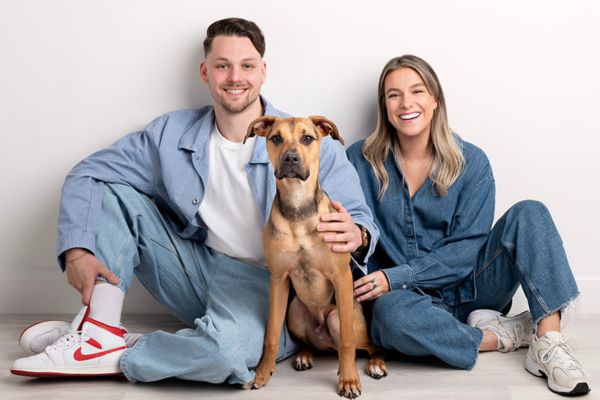 A portrait of a couple wearing denim and a dog sitting on the ground