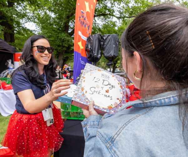 A lady wearing a red tulle skirt hands a lady a sock gift pack