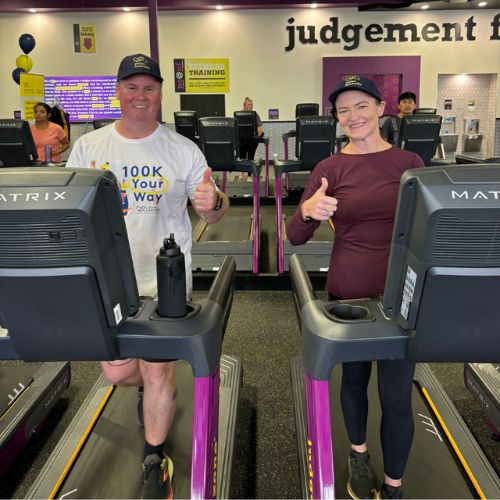 A man and a woman using treadmills at a Planet Fitness gym with their thumbs up