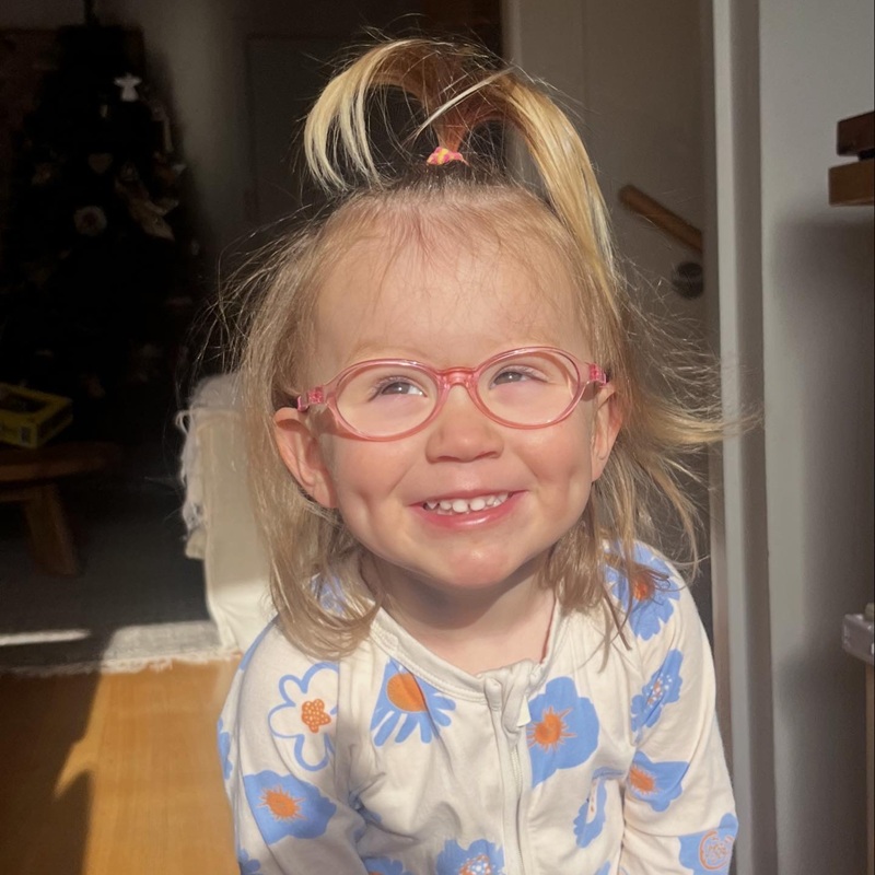 Young girl with blonde hair and pink glasses smiles widely