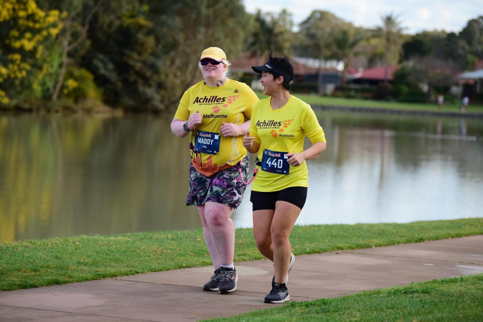 Two women wearing yellow shirts run along a path