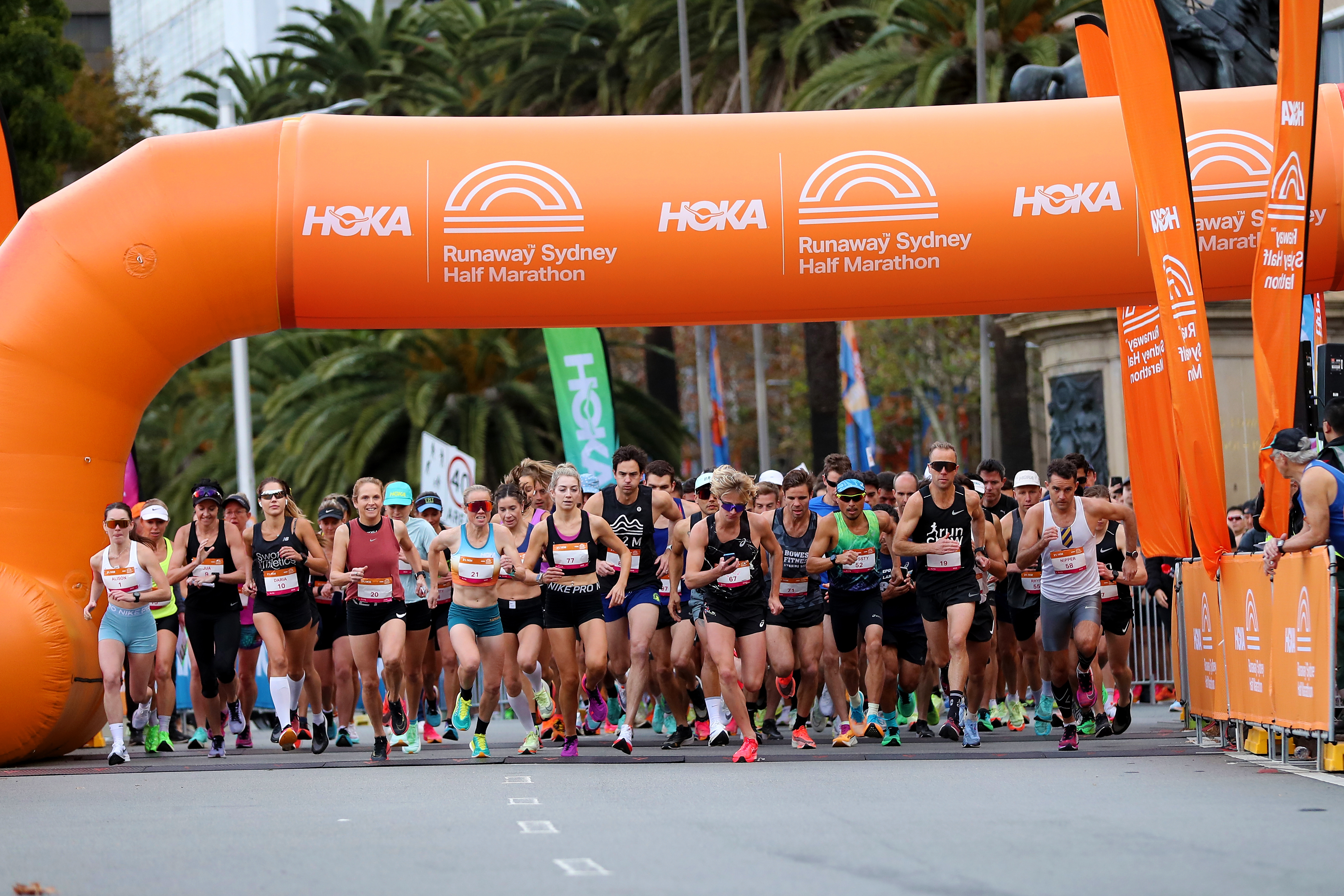 A group of runners under the orange start line at the Hoka Runaway Sydney Half Marathon