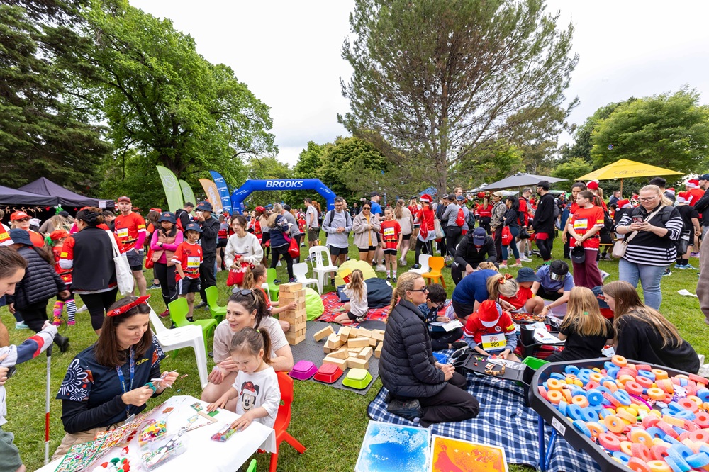A lively park scene with adults and children engaging in arts and crafts activities in the Santa Fun Run Village.