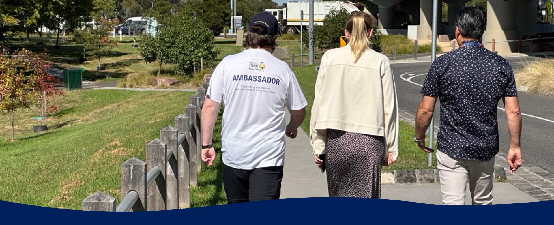 Three people walk side by side away from camera along a path